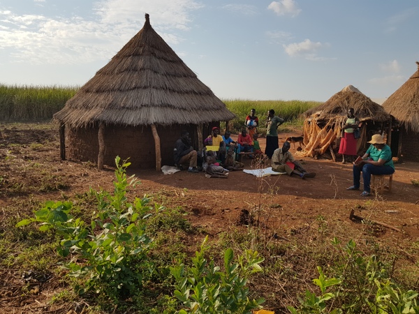 A family sit outside their home in Kiryandongo District. In the background, a few hundred steps from their house begins the vast sugarcane plantation. The Kiryandongo evictions have been halted by Lands Minister.