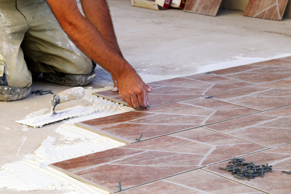 A man is laying tiles on the floor of a bathroom.
