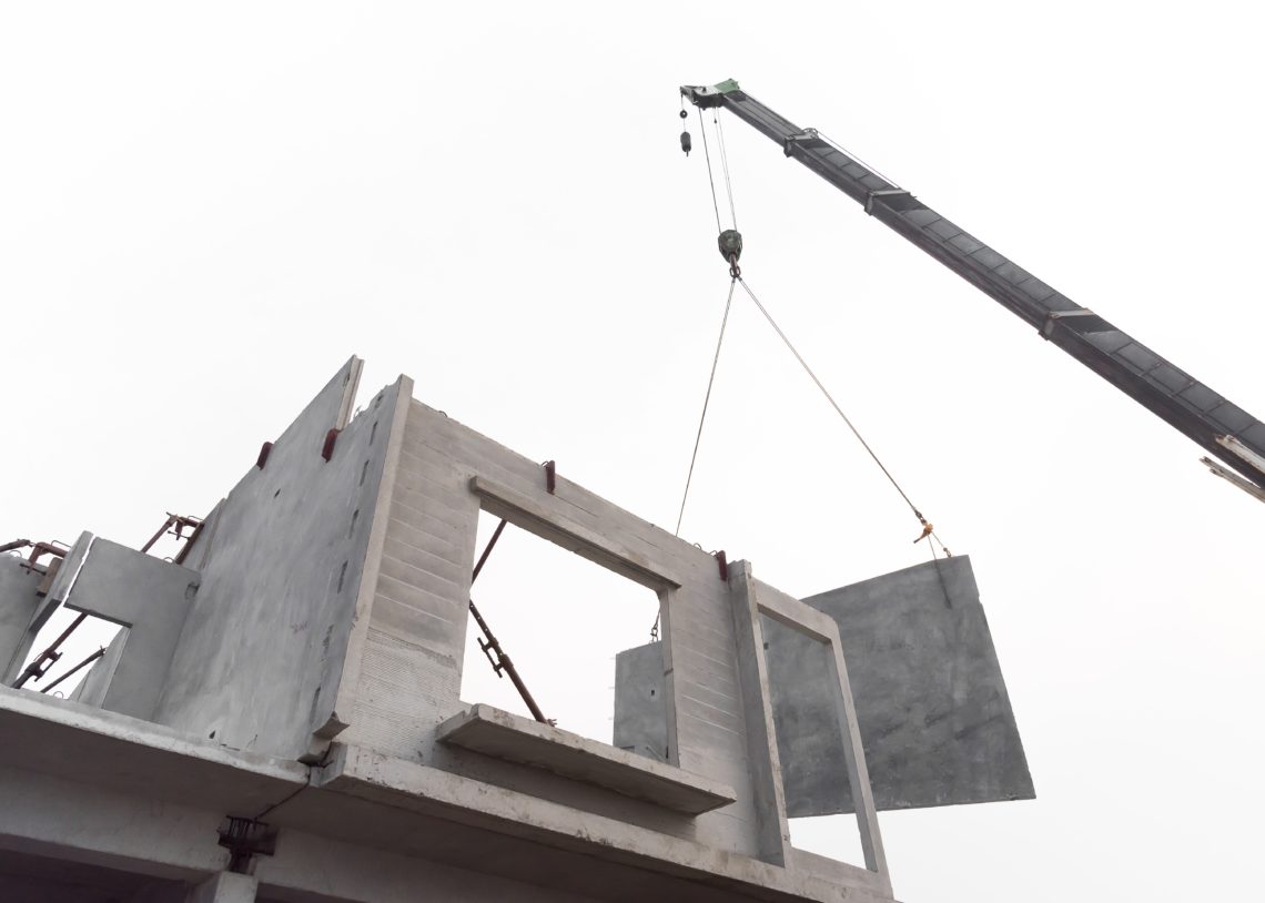Construction Site Crane Is Lifting A Precast Concrete Wall Panel To Installation Building.
